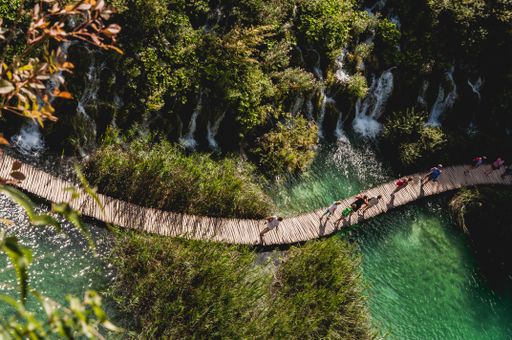 A high angle shot of a wooden bridge on a turquoise river surrounded  by greenery