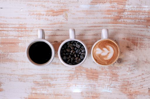 A high angle shot of three cups of different coffee on a wooden surface