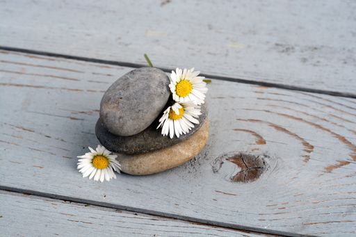 A closeup shot of three stones stacked on top of each other next to daisy flowers on a wooden surface