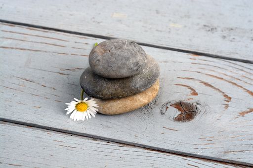 A closeup shot of pebbles stacked on top of each other next to Daisy flower on a wooden surface