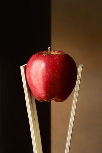 A vertical selective focus shot of a red apple between wooden sticks with a brown background