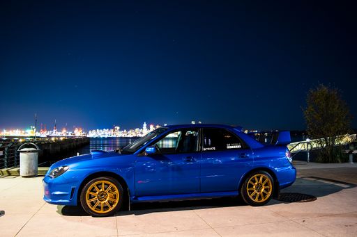 A beautiful shot of a blue Subaru car parked by the ocean at night in Vancouver, British Columbia, Canada