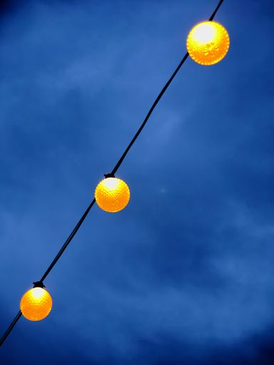 A low angle shot of lighting yellow round bulbs on an electric wire against blue cloudy sky