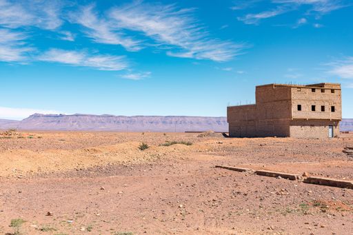 A brick house constructed at a desert in Morocco with mountains in the background