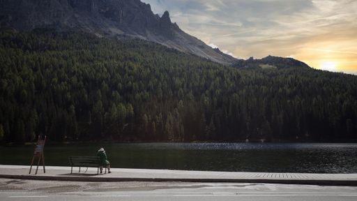 a Person sitting on bank in front of  Lago di Misurina during sundown.