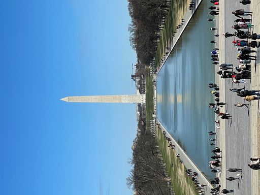 A vertical shot of the beautiful Washington Monument under a clear blue sky with tourists everywhere