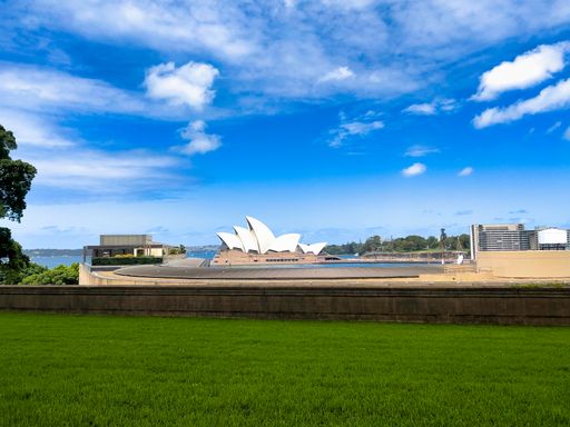 A beautiful shot of Sydney Opera House as seen from a far green grassland point under the clear blue sky, Sydney, Australia.
