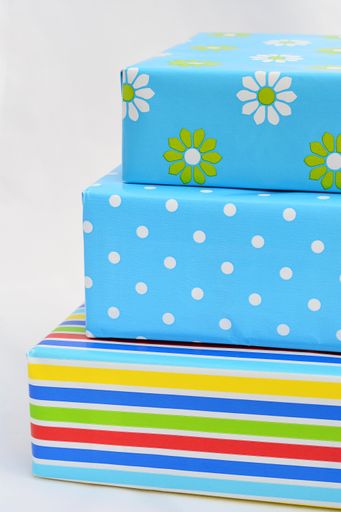 An isolated closeup vertical shot of gift boxes in colorful wrapping stacked on top of each other on white background
