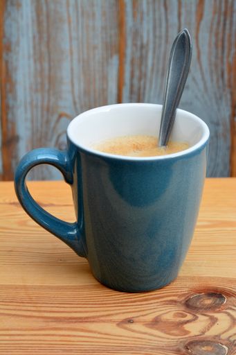 A vertical shot of a cup of hot coffee with a spoon in it on the table under the lights