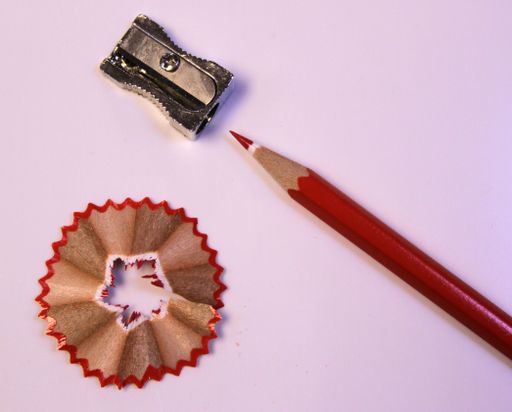 An isolated closeup shot of a sharp red pencil next to a metal sharpener with pencil shavings nearby