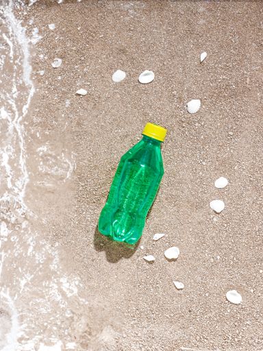 A vertical top view of a plastic green bottle put on a sandy beach