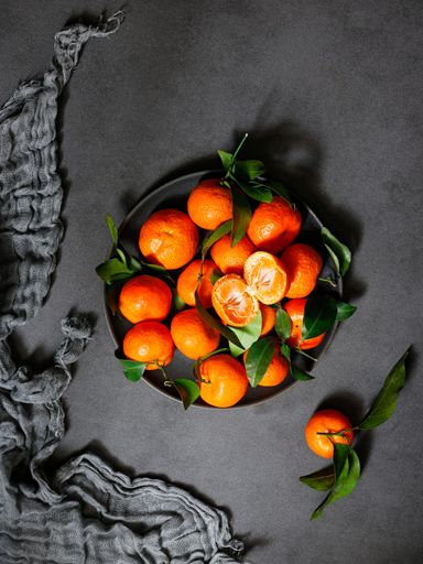 A vertical shot of tangerine with green leaves on a plate on a black aesthetic background