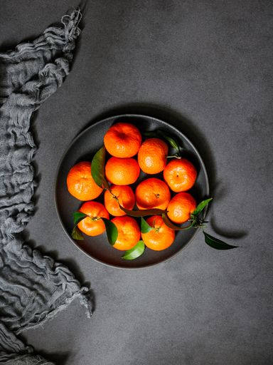 A vertical shot of tangerine with green leaves on a plate on a black aesthetic background