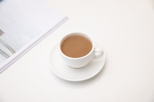 An overhead shot of a white cup filled with coffee on a saucer resting a white table