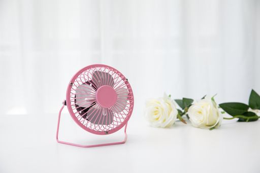 A pink small desk USB 4 blades cooling fan on a white table with roses in the background