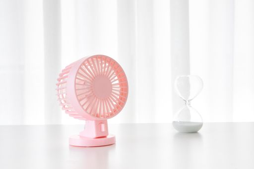 A pink metal mini fan and a sand hourglass on a white table