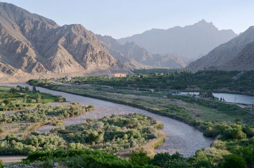 An aerial view of a landscape of a river surrounded by green field and mountains in the background
