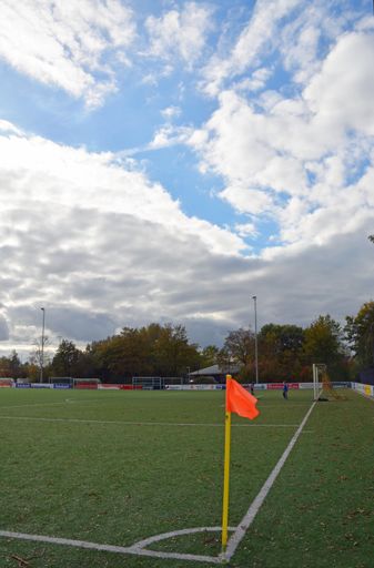A vertical shot of an orange flag in one angle of a soccer field under a blue cloudy sky