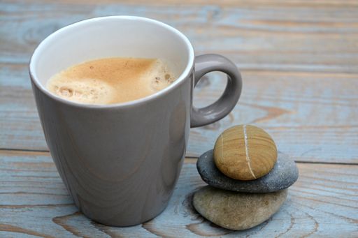 A closeup of a cup of coffee with flat stones on a wooden table under the lights