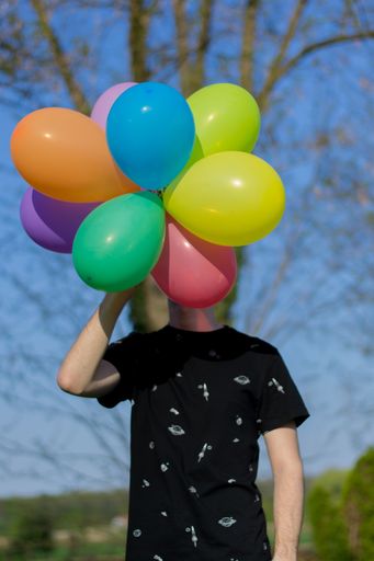A man wearing a black shirt and holding colorful balloons
