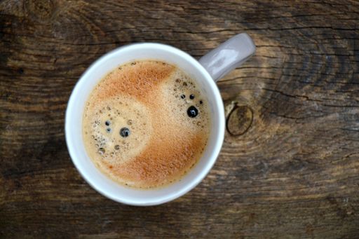 A high angle top view shallow focus closeup shot of coffee in a white mug on a wooden table