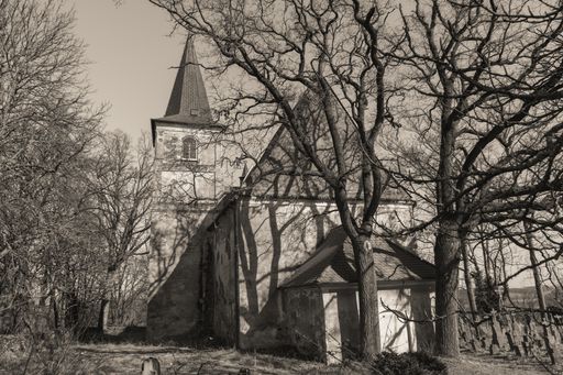 An old church in the graveyard surrounded by dry and bare trees in grayscale