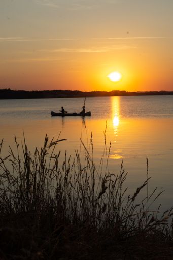 A vertical shot of a sunset view over the lake with a boat slowly gliding with two people