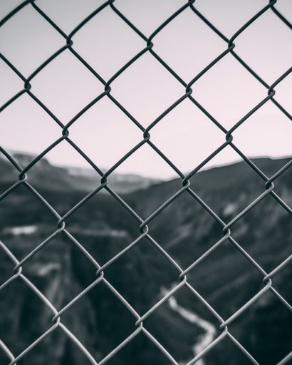 A vertical closeup shot of a metal fence against the blurry background of the hills