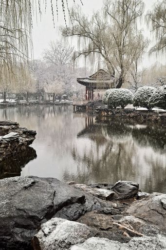 Chinese pavilion surrounded by pond and trees on snowy day, Beijing China. High 4K quality video.