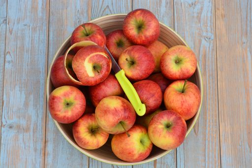 A high angle view of red apples with a knife in a bowl on the wooden table