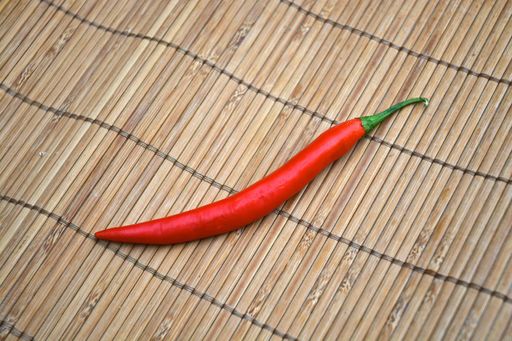 A high angle closeup shot of a red hot chili pepper on a bamboo table cover