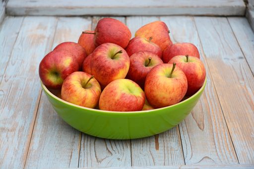 A closeup shot of red and yellow apples in a green plate on a wooden surface