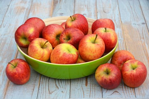 A closeup of red apples in a green bowl on the wooden table under the lights