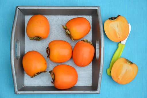 A high angle top view shot of persimmon fruits in and text to a gray tray on a blue tablecloth