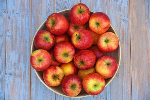A high angle top view shot of red and yellow apples in a plate on a wooden surface