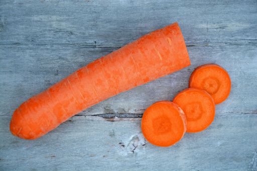 A high angle top view closeup shot of a carrot with three slices on a wooden surface
