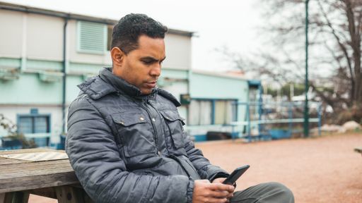 A Hispanic man sitting in winter clothes outdoors and using on his phone