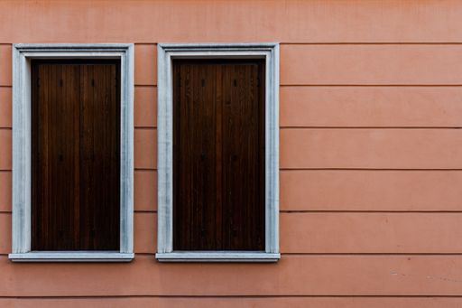 Two white windows covered with wooden boards of a pink building
