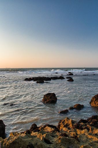 A vertical shot of a beautiful sea captured from a rocky shore during a scenic sunset