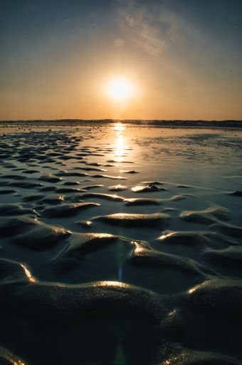 A vertical shot of the sun setting and reflecting on the surface of the ocean