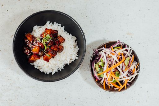 A top view of a bowl of vegetables and white rice topped with pork