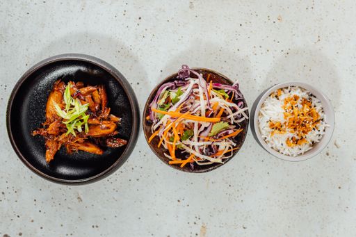 A top view of a bowl of vegetables, white rice, and meat on a white table