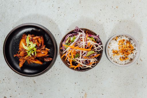 A top view of a bowl of vegetables, white rice, and meat on a white table