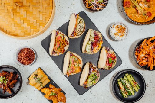 A top view of bao buns surrounded by different dishes on a white table