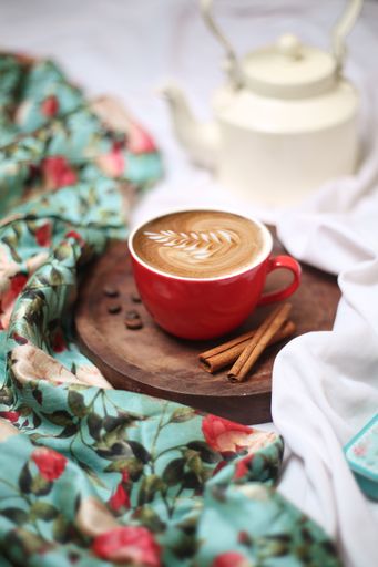 A closeup shot of a cup of coffee with cinnamon sticks on a wooden board