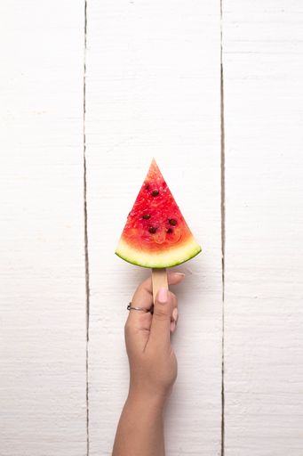 A slice of watermelon on a stick in a female hand isolated on a wooden background