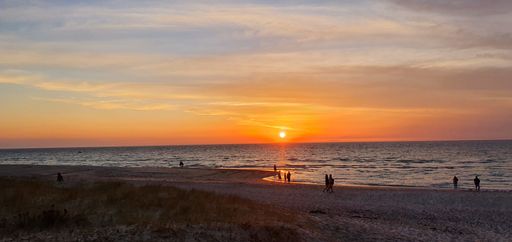 A scenery of sunset in the ocean with a silhouette of people walking on a sandy beach