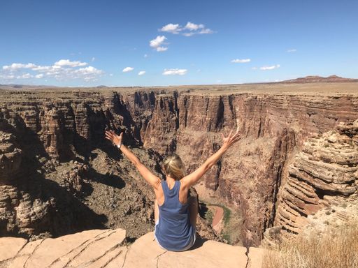 A young German girl from the back sitting with her arms up on the edge of a canyon and enjoying the view.
