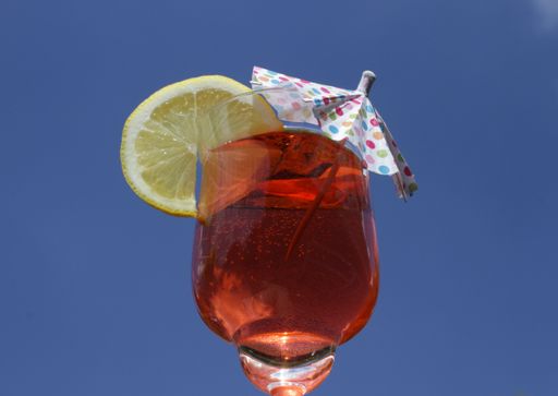 A low angle closeup shot of a translucent orange drink with a lemon slice and umbrella under the sky