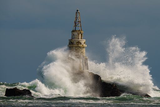 An old rusty lighthouse in the Black Sea with giant waves crashing on it in Ahtopol, Bulgaria